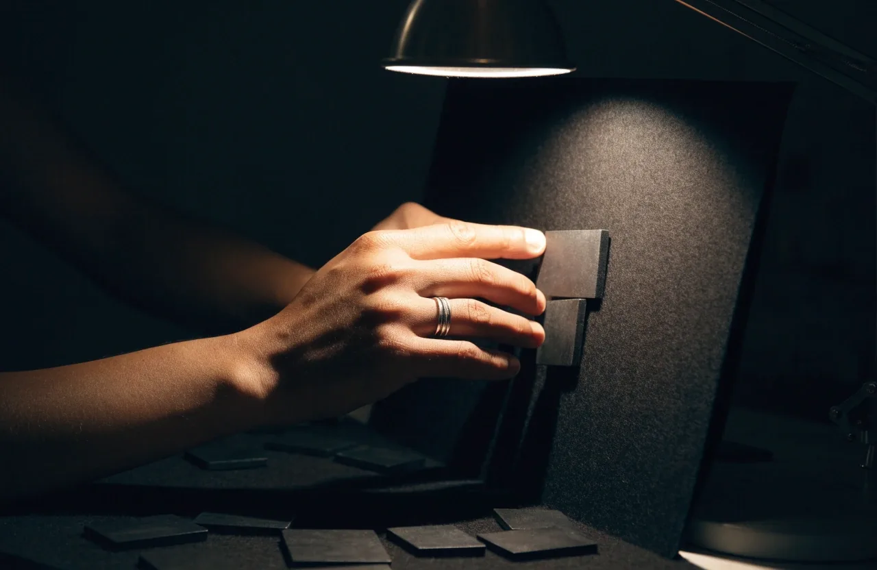Hands rearranging magnetic map tiles on a dark felt board under a work lamp